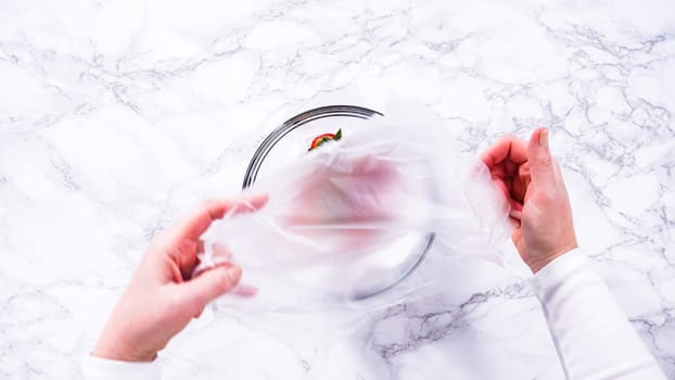 Flat lay. Strawberries, freshly washed and dried, are neatly stored in a glass bowl lined with a paper towel and securely covered with plastic wrap to maintain freshness.