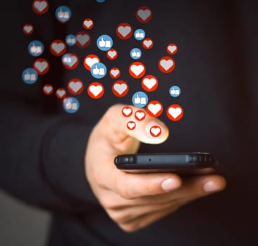 A young man holds a mobile phone in his hand and bank card, writes a positive review with likes and hearts or makes donate, uses social networks and does shopping, makes purchases with online banking.
