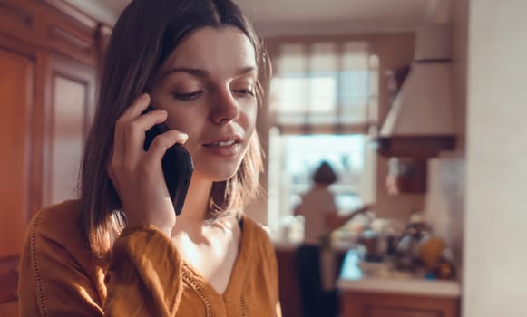 A young girl is talking on the phone with friends, communicating at home, against the backdrop of a cozy kitchen. A woman makes an order or purchase with home delivery, works remotely.