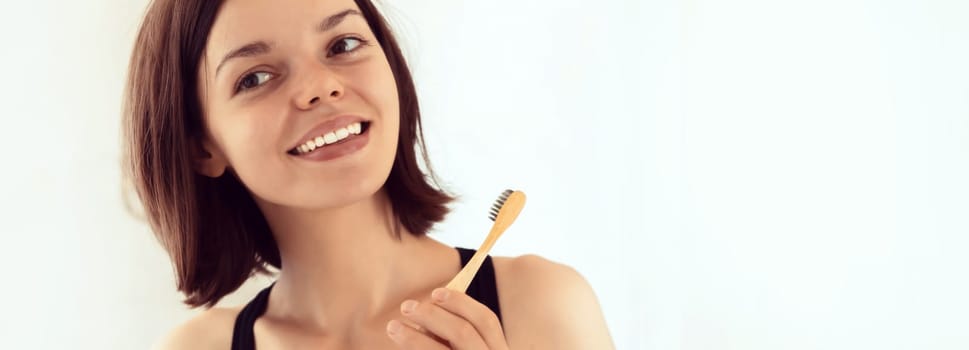 A young smiling girl brushes her teeth with toothpaste in the bathroom by the mirror in the morning, a woman takes good care of the health of tooth enamel and gums.