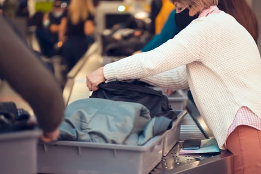 An elderly woman in line at the inspection of things on the checkpoint, security through a scanner before leaving for a flight at the airport or after arrival, a plastic box with luggage closeup.