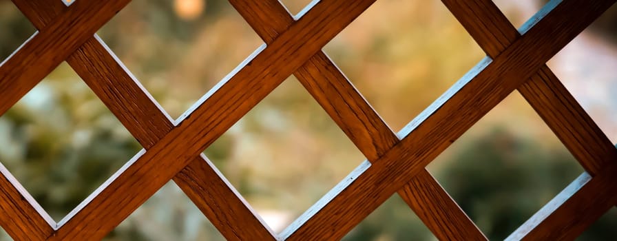A beautiful background with a wooden lattice, a square grid, a decorative fence on a balcony or terrace against the backdrop of a summer garden, an outdoor fence with a square, rhombic pattern.