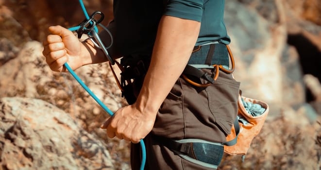 A young man belays for rock climbing in the mountains outdoors, an athlete controls on a rope during a workout, goes mountain climbing on a sunny day, close-up.