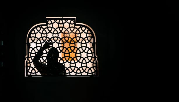 A Muslim girl in a black hijab stands behind a patterned wrought-iron fence. Woman in a conservative Arab country.