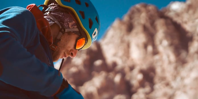 A man in special mountaineering glasses with a mirror-effect orange color, takes care of his eyesight and safety in the snowy mountains. The hiker travels in the mountains, is engaged in climbing.