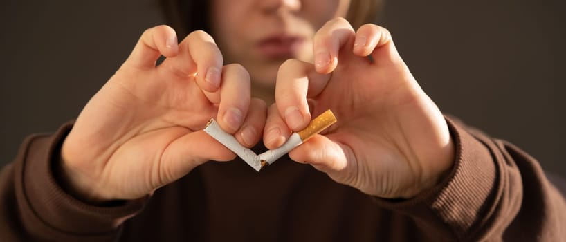 Young girl decisively breaks a cigarette in her hands, close-up view, a woman gets rid of nicotine addiction and chooses a healthy lifestyle, takes care of her beauty and health.
