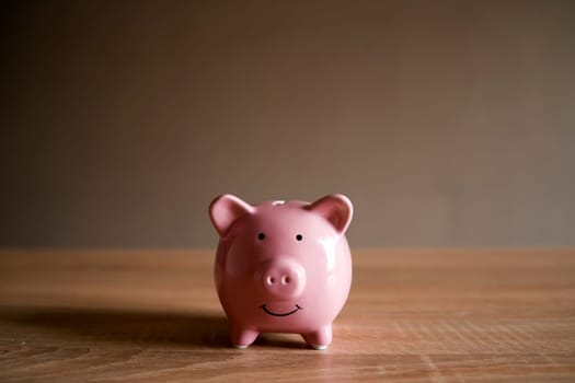 Piggy bank in the form of a smiling pink pig on the table to save wealth, savings and financial success, close-up view.