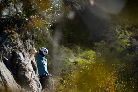 A young man is engaged in extreme sports, leads an active lifestyle, climbs a rock with climbing equipment in the sunny day against the background of Twin Caves, Leonidio, Arcadia, Greece.
