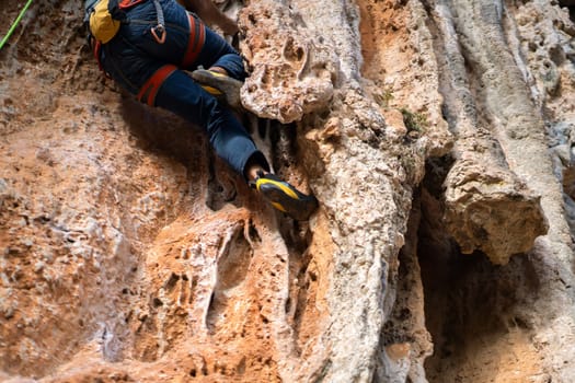 A young man with climbing equipment, in rock shoes, with a rope, magnesia, climbs the mountain up, is involved in rock climbing, mountaineering, extreme active sports.