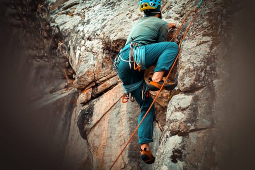 The young man is engaged in extreme sports, leads an active lifestyle, climbs a mountain, a rock with climbing equipment, wearing a helmet, with a rope, carabiners and climbing shoes.