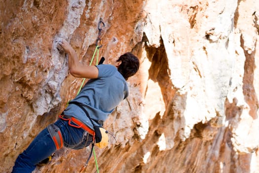 A young man with climbing equipment, in rock shoes, with a rope, magnesia, climbs the mountain up, is involved in rock climbing, mountaineering, extreme active sports.