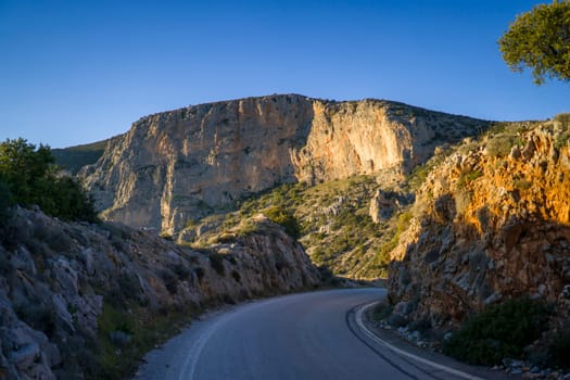 Beautiful road among the rocky yellow-red mountains on the southern mediterranean coast in the rays of the sun at sunset.