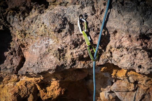A carabiner, quickdraw with bright blue rope at a climbing way to a station in rocky mountains.