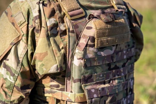 Bulletproof vest, plate carrier in camouflage colors worn over military uniform on a soldier close-up, tactical man takes care of his safety during military operations and outdoors training.