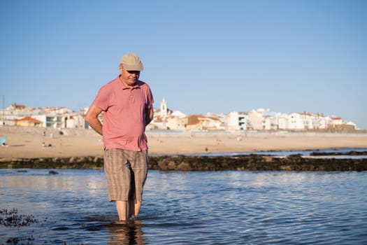 An elderly man with a mustache walking on the beach
