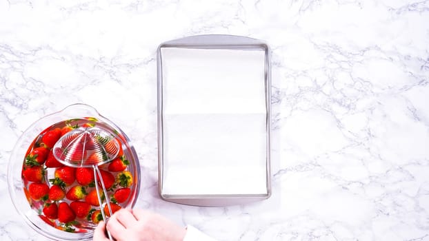 Flat lay. Juicy red strawberries, freshly washed, are spread out to dry on a baking sheet, carefully lined with paper towels to absorb excess moisture and prevent mold.