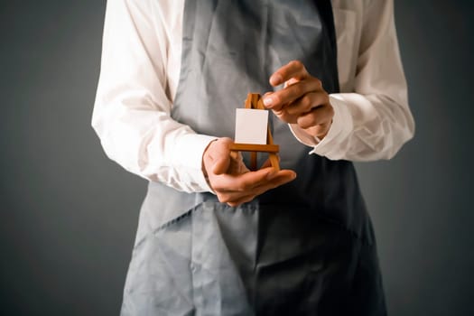 The male artist's hands are holding a miniature easel with a small piece of white paper on it. A creative idea for inviting and discovering art.
