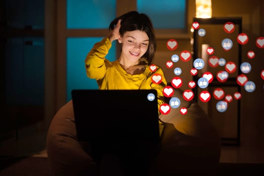Joyful young girl working on a laptop at night at home, happy with a success and rating, woman reacts emotionally with gestures on feedback from people through social networks, heart signs around.
