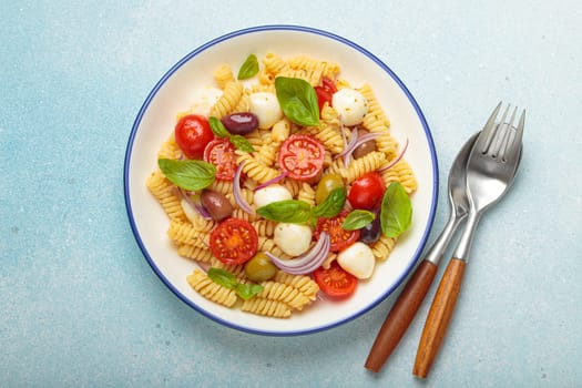 Plate with Italian fusilli pasta salad with fresh cherry tomatoes, mozzarella, olives, red onion, and basil leaves, concept of Italian culinary tradition