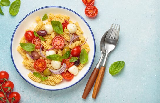 Plate with Italian fusilli pasta salad with fresh cherry tomatoes, mozzarella, olives, red onion, and basil leaves, concept of Italian culinary tradition