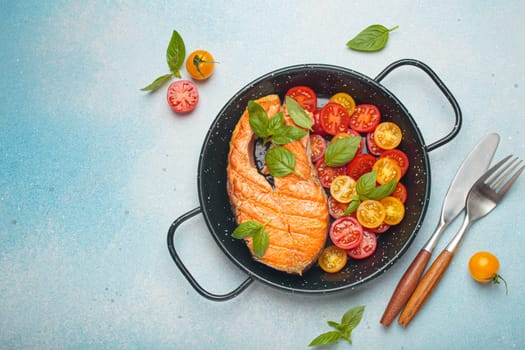 Grilled salmon steak on a black pan, accompanied by vibrant cherry tomatoes and fresh basil leaves, healthy eating or diet concept, copy space