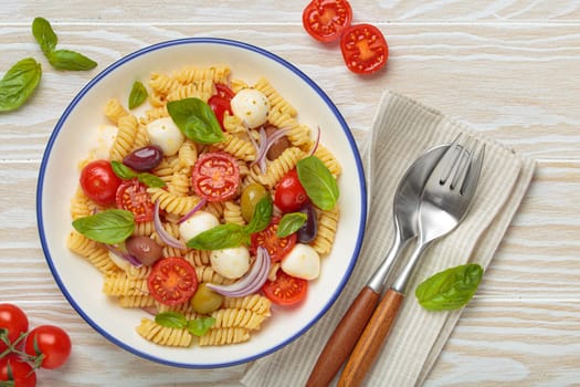 Plate with Italian fusilli pasta salad with fresh cherry tomatoes, mozzarella, olives, red onion, and basil leaves, concept of Italian culinary tradition