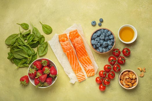 Raw salmon fillets, spinach, strawberries, blueberries, cherry tomatoes, almonds and olive oil. Set of foods that help to reduce inflammation, top view
