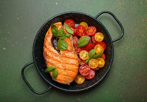 Grilled salmon steak on a black pan, accompanied by vibrant cherry tomatoes and fresh basil leaves, healthy eating or diet concept