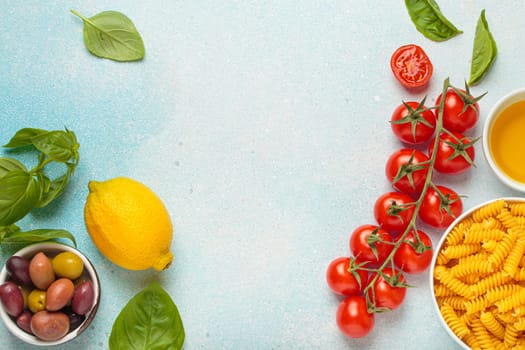 Fresh ingredients for preparing a traditional Italian pasta dish are arranged on a light blue background, fusilli pasta, fresh tomatoes, basil, olives, lemon and olive oil, copy space