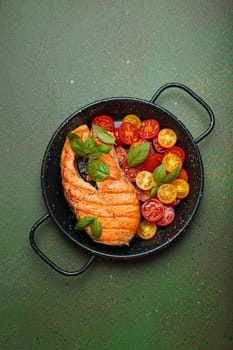 Grilled salmon steak on a black pan, accompanied by vibrant cherry tomatoes and fresh basil leaves, healthy eating or diet concept