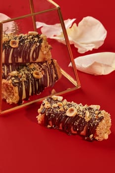 Sweet hazelnut and chocolate mini cakes are reflecting in a golden glass box on a red background with petals
