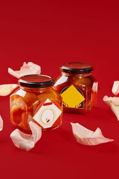 Two luxardo baba al maraschino jars surrounded by rose petals on a vibrant red background, creating a luxurious and romantic atmosphere