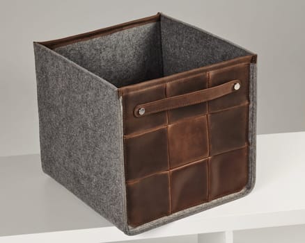 Stylish brown leather and gray felt storage box resting on a white shelf, ideal for organizing belongings