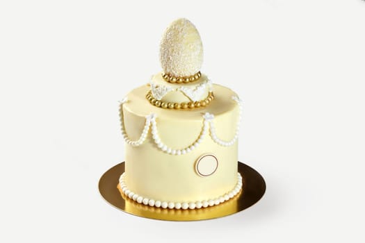 Small elegant easter cake decorated with white chocolate egg, pearls, and golden decorations