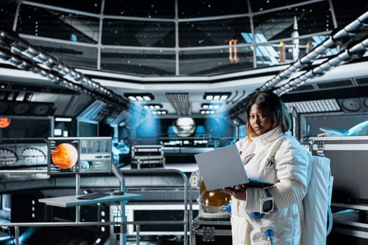 Female cosmonaut monitoring system diagnostics on laptop before Mars expedition. African american astronaut in spaceship explores red planet to support human life beyond Earth