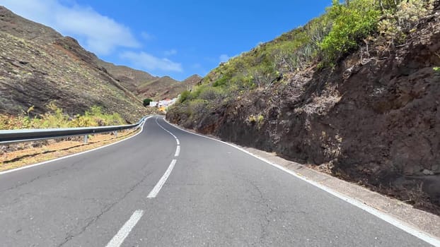 A scenic view of a winding road surrounded by majestic mountains and lush greenery under a clear blue sky