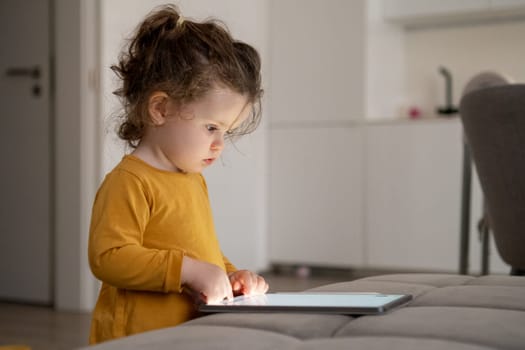 Young girl focused on digital drawing on a tablet. Cozy family space in the background.