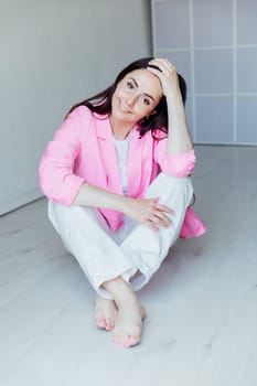 Beautiful fashion brunette woman in white clothes and pink jacket sitting on the floor