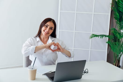 Business brunette woman showing her hands heart at desk in office