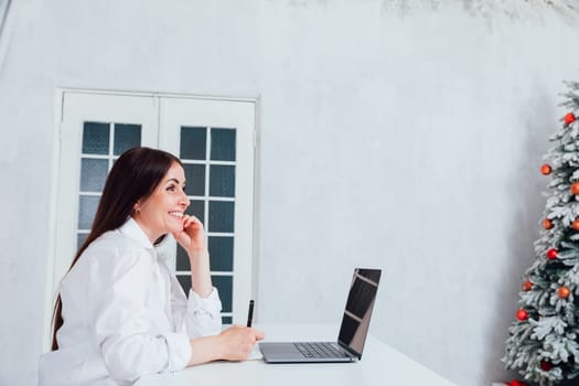Business brunette woman working on laptop at office desk near christmas tree
