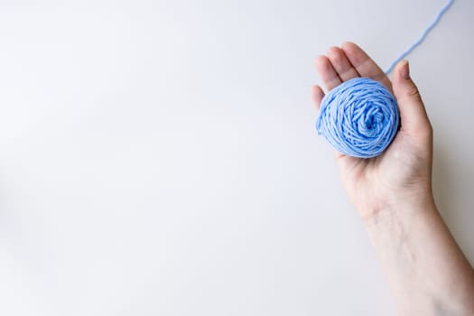 Female hand holding blue yarn ball on white background. High quality.