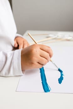 Young caucasian child painting with blue brushstroke on white paper.