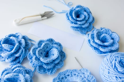Blue crocheted flowers with yarn and tools on white background. High quality.
