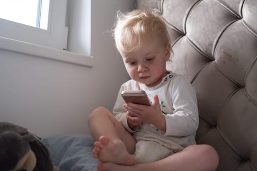 A toddler girl sitting on the couch with her mom phone.