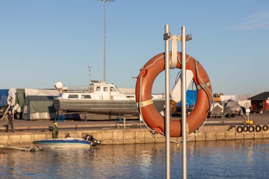 SOS nautical emergency concept. Lifebuoy, orange lifebelt put on vertical ready for using. Close up circle lifesaver buoy at Finnish marina