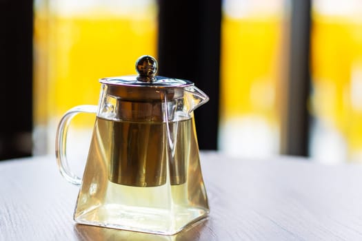 A beautiful glass teapot is resting elegantly upon a rustic wooden table, creating a warm and inviting ambiance in the room
