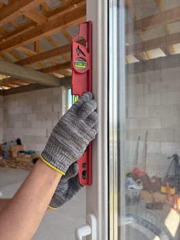 A construction worker's hands check a window frame with a level, ensuring accurate alignment and structural integrity during a remodel or building construction project.