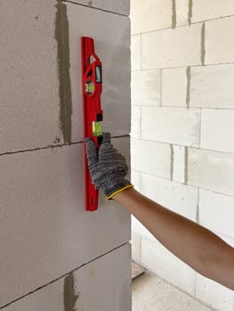 A builder applies a bubble level to a new wall at a construction site to check its levelness. Measuring tools at the construction site.