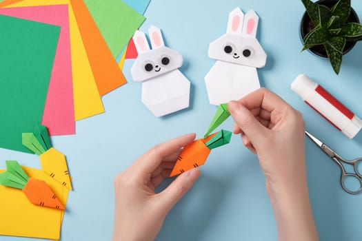 Women's hands make paper origami carrot. Around paper crafting tools. DIY project concept for children, hobby and creativity.