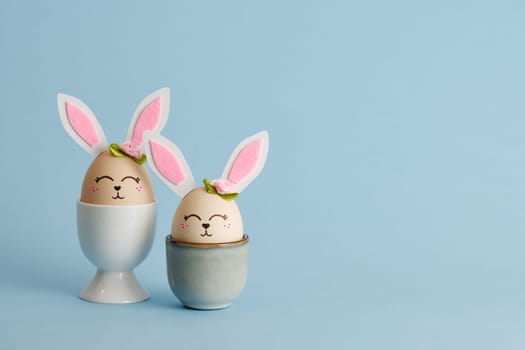 Cute Easter bunny shaped eggs in egg holders on blue background. Place for your text